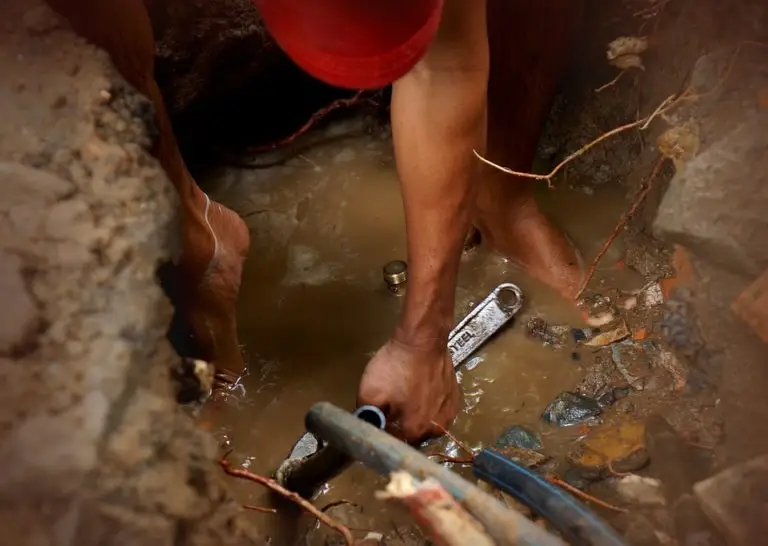 plumber digging into wet ground for Houston sewer repair