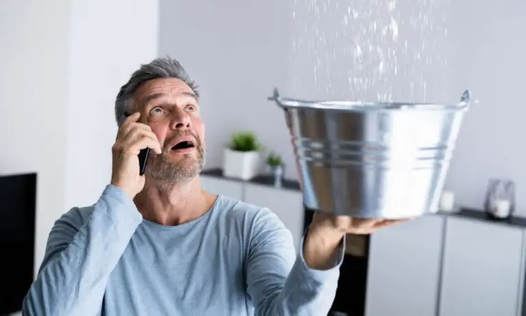 man catching water with a bucket while phoning for Houston plumbing leak repair
